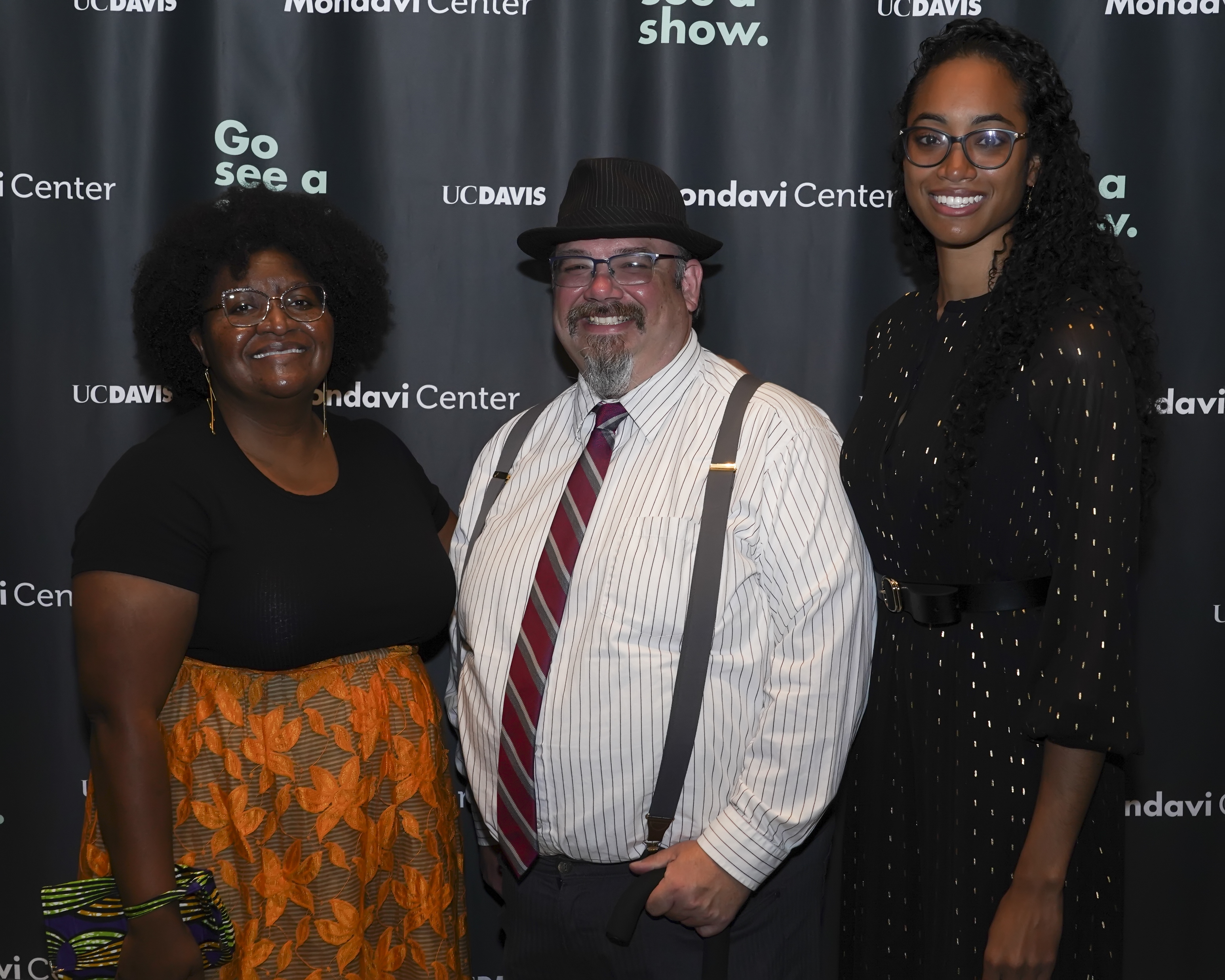 Three people smiling and posing in front of a backdrop with text "UC DAVIS," "Mondavi Center," and "Go see a show."