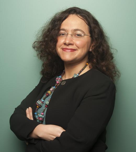 headshot of Mariel Vázquez standing against a green wall with arms folded across her chest