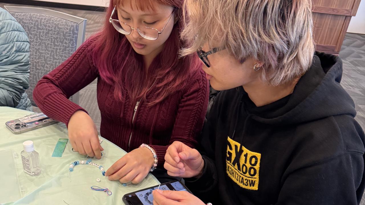 two students sit at table making bracelets at de-stress event
